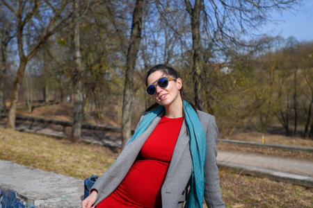 Pregnant girl in a red dress in the park. Portrait of a beautiful pregnant woman in a red dress and...