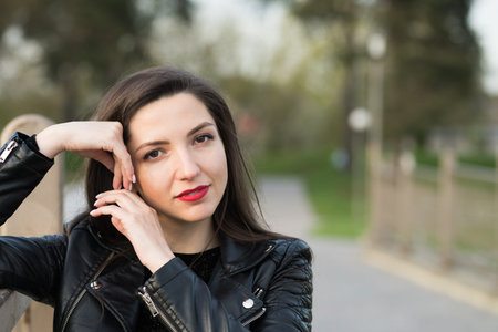 Beautiful brunette in a black jacket and red lips close-up. Closeup of street style fashion Portrait...