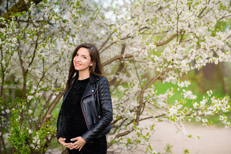 Pregnant girl in the flowered garden. beautiful pregnant girl in a black dress is standing in a...