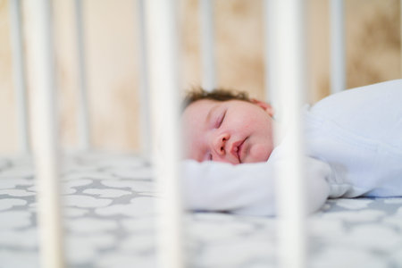 The baby sleeps in the crib. A charming baby sleeps in a crib for sleeping attached to the bed of...
