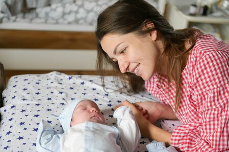 mother looks at her child. Young mother looking on her newborn baby. Beautiful mom lying at bed with a cute sleeping new born child. Baby's first days of life in family at homeの写真素材