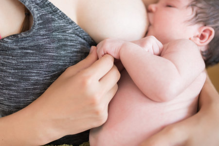 Mother breastfeeds baby. Mother breastfeeding her newborn baby beside window. Milk from mother's...