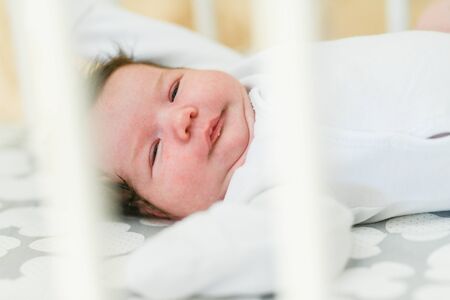 The baby sleeps in the crib. Charming girl sleeps in a bed for sleep, attached to the bed of parents. A small child having a nap in the crib. Baby in the sun nursery.の写真素材
