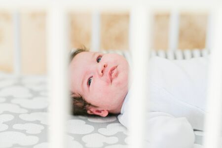 Baby in the crib. Newborn baby boy in bed. New born child sleeping under a white knitted blanket. Children sleep. Bedding for kids. Infant napping in bed. Healthy little kid shortly after birth. Cable knit textileの写真素材