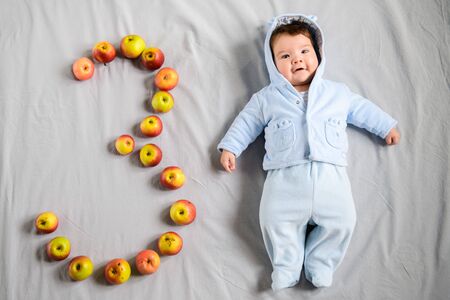 Three month old baby. three month old baby, on a gray background. laid out the figure three of applesの写真素材
