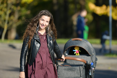 Portrait of mom with a stroller. Portrait of a beautiful young woman pushing a stroller in a park....