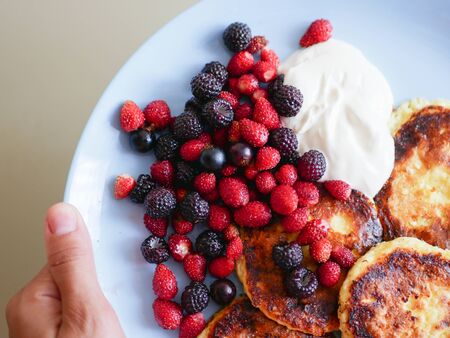 Cheesecakes with berries. and sour cream. Cheesecakes served with lots of fresh berries on a white plate. Gourmet breakfast - curd cheesecakes, curd pancakes with raspberries, strawberries, blueberries. Close. healthy food, healthy breakfast. on a blue plate.の写真素材