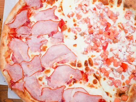 pizza with red fish and ham. divided into two components. the dough is cooked in a clay oven. on a wooden table. Close up of italian pizza. Ham, bacon, yellow cheese, tomato sauce. Top view, flat lay.の写真素材