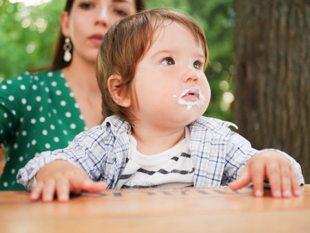 mom feeds her baby on the street. A mother feeds her little baby with a spoon on the street. mouth in food. healthy cottage cheese and yogurd.の写真素材