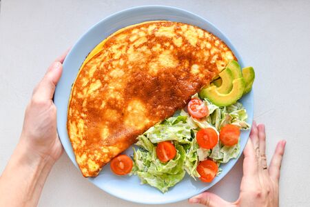fried eggs with vegetables. hands in the frame. Vegetable omelet on a blue plate on a white table, top view.の写真素材