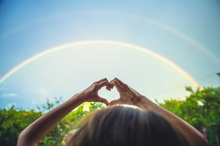 symbolism of love, rainbow sky, love. heart shaped hands and rainbow in the sky. double rainbowの写真素材