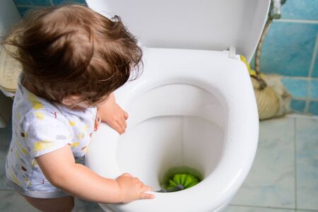 the child cleans the toilet. Child labour. Little girl cleans the toilet. toilet brush. grooming yourself. training a child for cleaningの写真素材