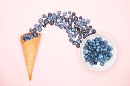 Fresh blueberries in ice cream cone on a pink background. Blueberry Blast. Summer vacation concept. Flat lay, top view. The style of natural organic food. hands picking blueberriesの写真素材