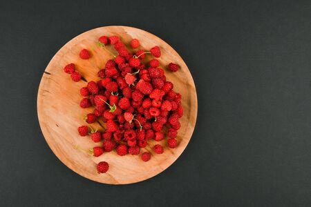 Raspberries on a wooden plate. On a black background close-up. wooden tray. view from above. place for writing. Fresh raspberries on a dark stone background. Close Selective Focusの写真素材