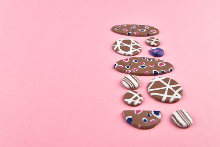 A product from polymer clay. Hand sculpting, product for earrings on a pink background. View from above. Beige earrings with colorful patterns. Handmade polymer clay jewelry.の写真素材