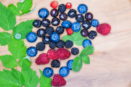 Wild berries on a wooden plate. Composition of three types of summer berries lying on a textured...
