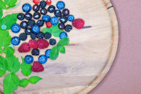berries on a wooden plate. Composition of three types of summer berries lying on a textured wooden...