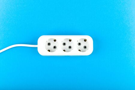 White socket with wire. View from above. on a blue background. White socket and extension cord. Extension cord for three outlets with a long spiral cordの写真素材