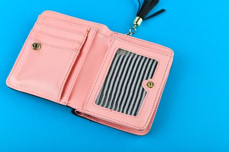 Pink wallet on a blue background. Wallet with a black tassel. A place to write. Close-up. Pink leather wallet isolated on a blue background. Minimalismの写真素材