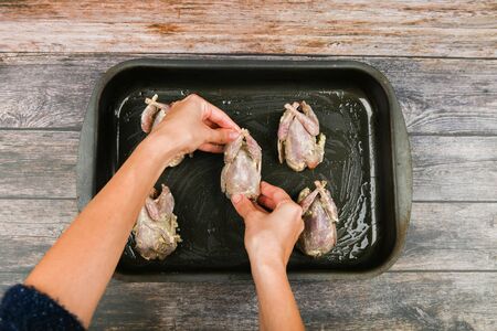 Quail on a wooden background. Quail baking on a baking sheet. cooking quail. Lies on the forehead, in front of the oven. close-up. hands in cooking.の写真素材