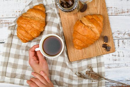 Girl holds a coffee mug. on the background of a croissant. coffee with a croissant. the beginning of the morning. Coffee cup. Top view on woman's hands holding a cup with coffee and fresh french croissant.の写真素材