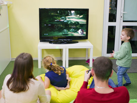 Kiev, Ukraine- March 10, 2019 - Mom and Dad play a game console at home. Children play next to them....