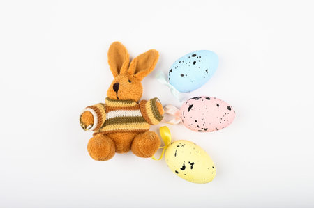 Brown plush hare with easter eggs on a white background. Multi-colored eggs dotted