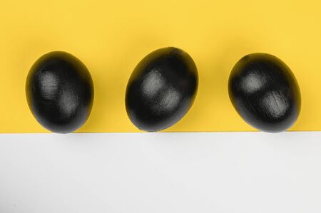 three black eggs on a yellow-white background. flat lay. Black Easter. three black eggs.の写真素材