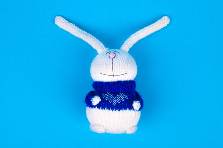 White knitted rabbit, in a blue jacket with a heart, on a blue background. Rabbit with a heart....
