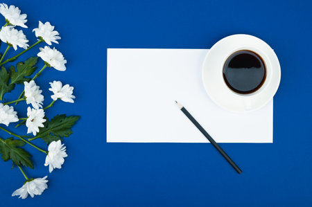 Female workspace. A cup of coffe and flowers frame on blue background. Copy space.