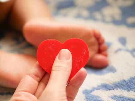 mother holds heart on the background of a small child.の写真素材