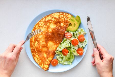 fried eggs with vegetables. hands in the frame. Vegetable omelet on a blue plate on a white table, top view.の写真素材