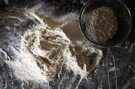 Colander with flour on the table. Stainless Steel Fine Mesh Strainer Colander Flour Sieve with Handle on dark background poudered with flour. Kitchenware.の写真素材