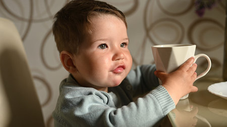Little child drinks water from a mug on his own. Independent baby