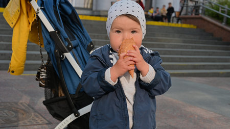 1-2 year old child eats ice cream on the street. stroller background