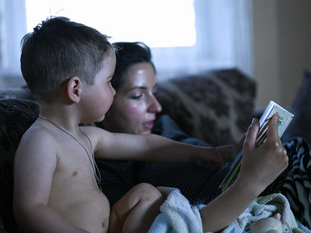 Mom with a child reading a book in front of the TVの写真素材