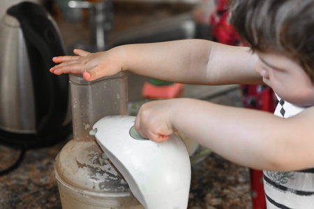 Little child helps mom in the kitchen with cooking, whipping food in a combine.