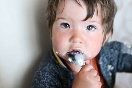 child with a spoon in his mouth looks at the cameraの写真素材