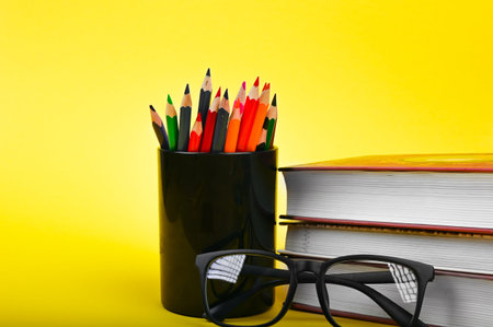 glasses with pencils and a book on a yellow background. High quality photo