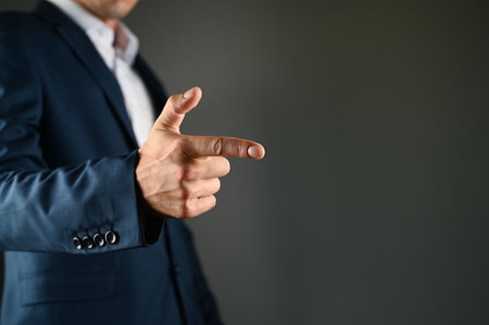 The man holds his index finger in front of him. A man in a suit points a finger forward on a black background. Concept: click on the button, specify specify. High quality photoの写真素材