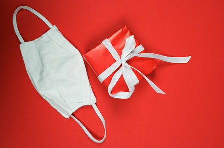 Red gift box and protective mask on red surface with copy space. Christmas and New Year holidays during quarantine. ... High quality photoの写真素材