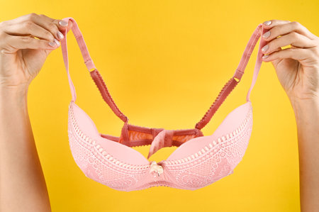 Hands holding a bra on a yellow background. High quality photoの写真素材