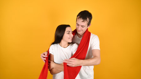 Lovely young couple hugging. Portrait of happy young couple with red warm scarf on yellow background. Valentines Day celebrationの写真素材