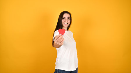 Young woman with heart in hands, on a yellow background. High quality photoの写真素材