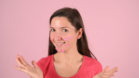 Young woman worried about acne and irritation on the skin, on a pink background. High quality photoの写真素材