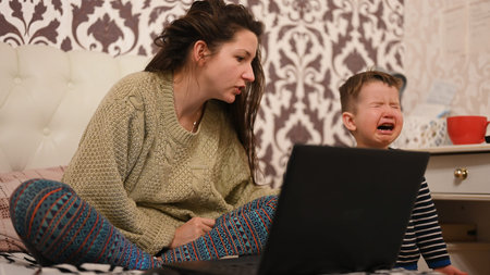 Mother works at the computer, the child is crying. High quality photoの写真素材