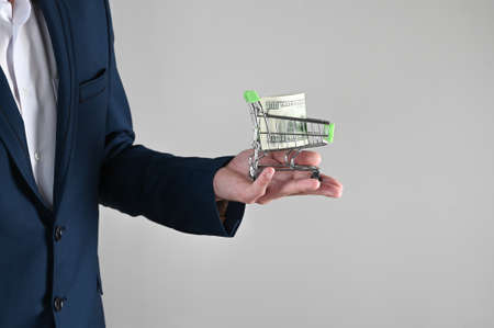 a man in a suit holds a shopping cart in his hands with dollars. High quality photoの写真素材
