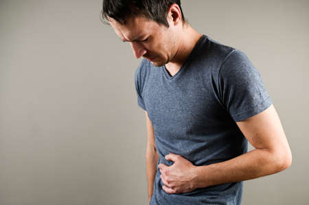 Man in pain holding his hurting stomach isolated on the gray background. Abdominal pain. High quality photoの写真素材