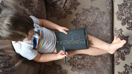 Cute Caucasian boy with draws on tablet, sitting on the sofa. High quality photoの写真素材