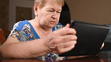 An elderly woman watching the news at her tablet.